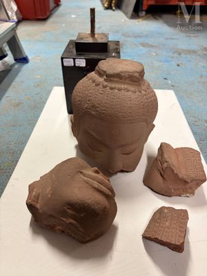 une sculpture en argile représentant une tête, posée sur une table à côté de rochers