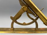 un télescope ancien en laiton posé sur un socle en bois, sur fond blanc