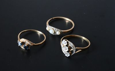 three gold rings with diamonds and a pearl on a black surface