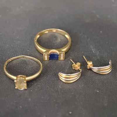 trois bagues en or et une bague ornée d'une pierre bleue sur un fond noir
