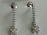 two pairs of diamond earrings on a white surface with a price tag