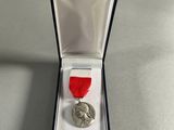 a silver medal with a red ribbon in a black box