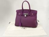 sac à main en cuir violet posé sur une serviette blanche, sur une surface blanche