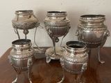 five silver vases sitting on a table with a clock in the background