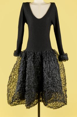 une robe noire posée sur un présentoir à mannequin, sur fond jaune