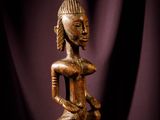 une statue en bois posée sur une table, à côté d'un rideau violet