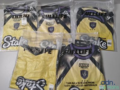 Trois sacs contenant des t-shirts jaunes ornés de logos noirs et blancs sont posés sur une table
