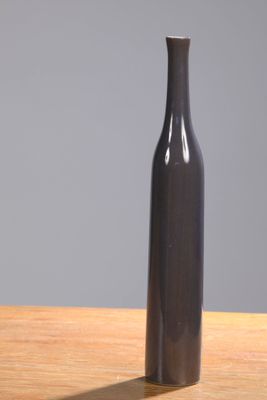 a black vase sitting on a wooden table with a gray wall in the background