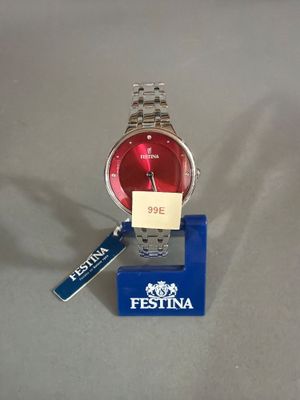 une montre rouge posée sur un socle bleu, avec une étiquette accrochée dessus