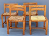 four wooden chairs with woven seats sit in front of a gray wall