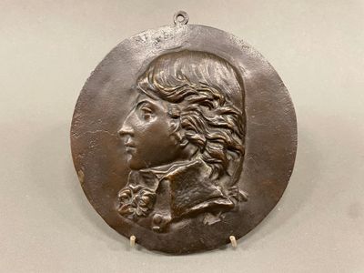 une image représentant un médaillon en bronze à l'effigie d'un homme aux cheveux longs