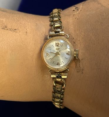 une personne porte au poignet une montre en or sur fond bleu