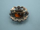 sterling silver broochle with orange stone in center on blue background