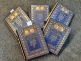 Quatre livres bleus sont posés sur un tapis bordé d'or.