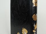 an old black book with gold flowers on it sitting on a white surface