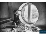 black and white photograph of a woman sitting on a bed in front of a round window