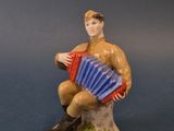 une figurine représentant un homme assis sur un rocher, un accordéon à la main