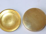 two gold metal plates sitting side by side on a white surface
