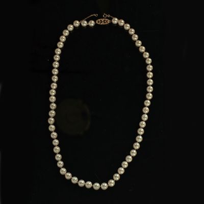 a white pearl necklace with a gold clasp on a black background