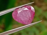 une personne tenant une pince sur laquelle est fixée une pierre rose en forme de cœur