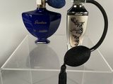 two perfume bottles on a clear shelf with a blue vase in the background