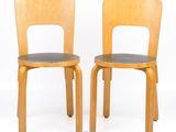pair of wooden chairs with black leather seats against a white background