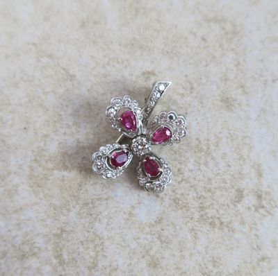 un gros plan sur une broche en forme de fleur, sertie de diamants et de rubis
