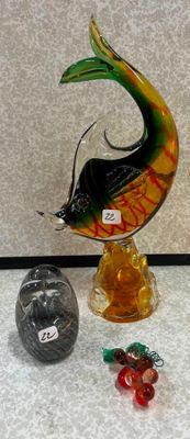 une sculpture en verre représentant un poisson, posée sur un socle à côté d'autres objets en verre