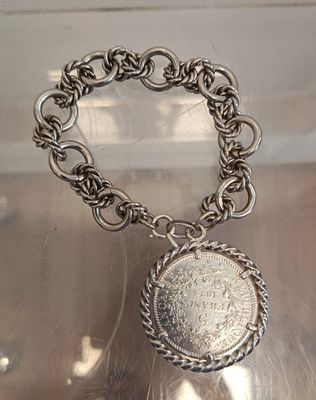 silver bracelet with a coin on a chain on a table