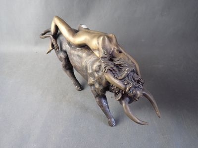 bronze statue of a woman laying on a bull on a gray background