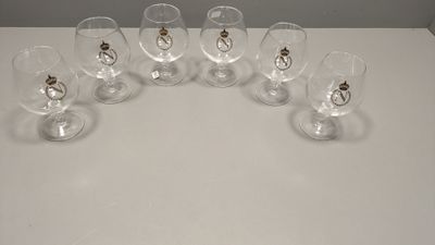 six verres à vin vides posés sur une table, avec un anneau doré sur le bord