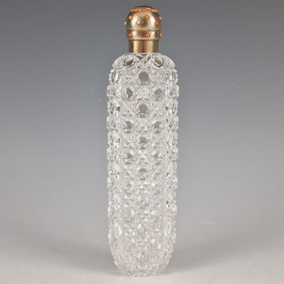 une bouteille en verre transparent avec un bouchon doré, posée sur une surface blanche