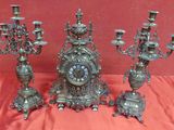 five silver candlesticks and a clock sitting on a red cloth