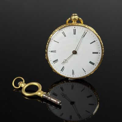 a gold pocket watch with a key on a black surface