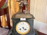 a clock sitting on a table with a statue on top of it