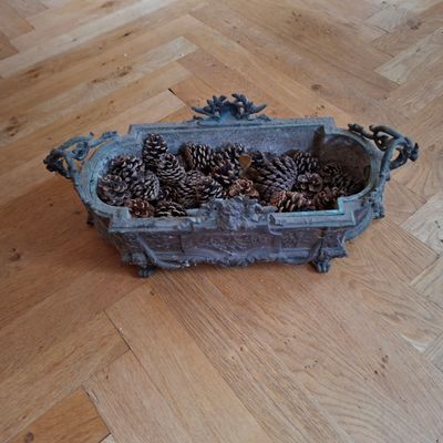des pommes de pin dans un récipient en métal posé sur un plancher en bois