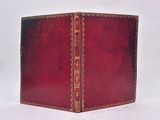 an old book with a red cover sitting on top of a white surface