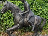 une statue représentant un homme à cheval devant une haie