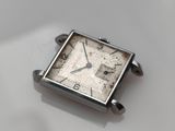 a silver square watch sitting on a white surface