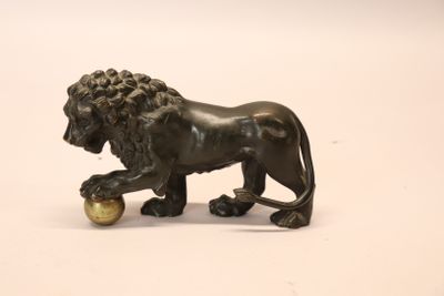 une statue en bronze représentant un lion tenant une balle entre ses pattes