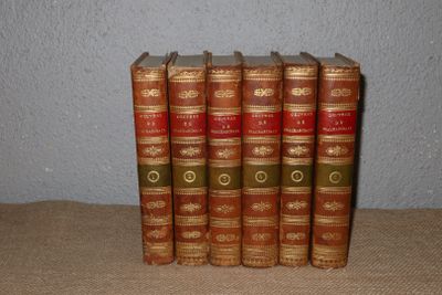 five old books are lined up on a table in a row