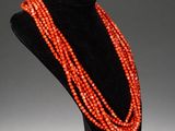 an orange beaded necklace on a black mannequin stand