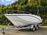 a small white boat on a trailer parked in the grass
