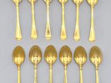 six gold plated spoons and two silver spoons on a white surface
