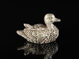 a silver duck figurine sitting on top of a black surface