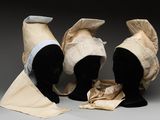 trois têtes de mannequins coiffées de chapeaux, exposées sur une surface grise