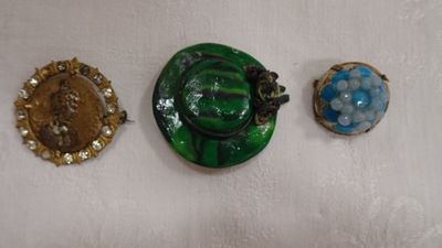 Trois broches de couleurs différentes sont exposées sur un fond blanc