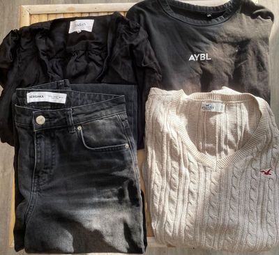 Deux paires de jeans et un pull sont posés sur une étagère en bois.