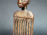 une image représentant un peigne en bois surmonté d'un visage sculpté