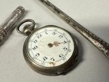 a silver pocket watch and a silver key on a table